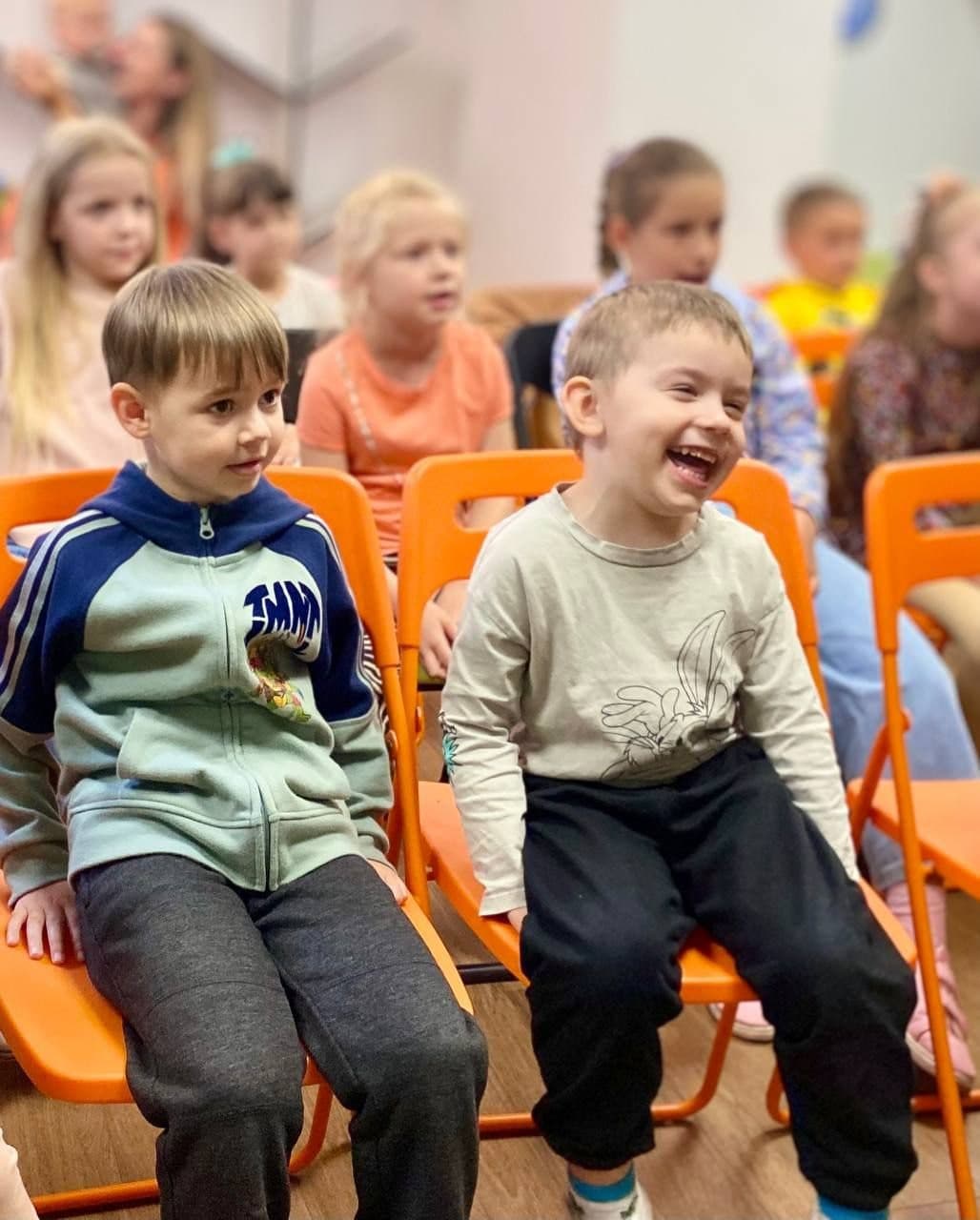 Two young boys laugh and watch from their seats in the audience.