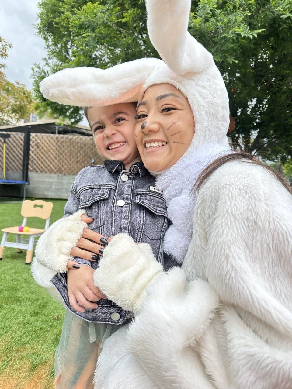 A smiling child is held by a friendly bunny-costumed performer in a garden.
