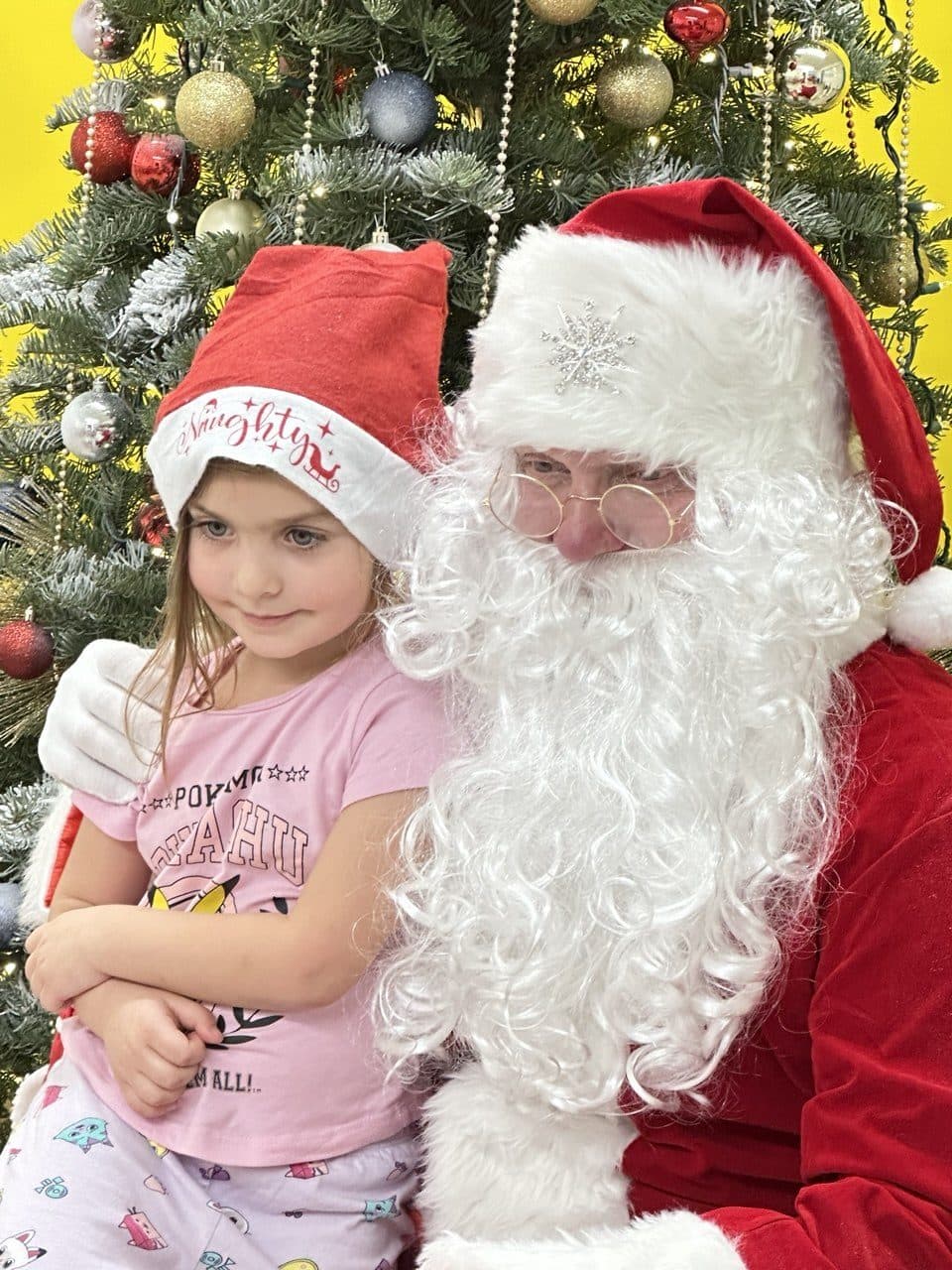 A young child sits on Santa's lap in front of a decorated tree.