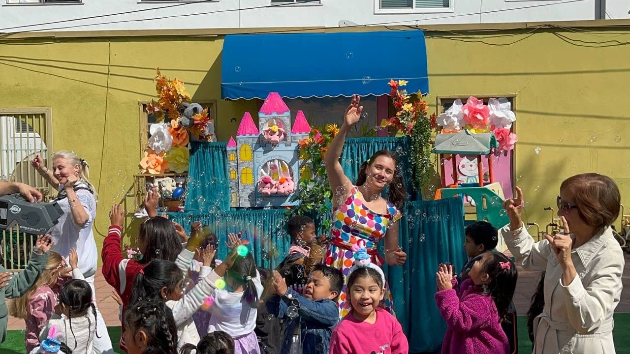 A group of laughing children cheers and reaches up amid bubbles.