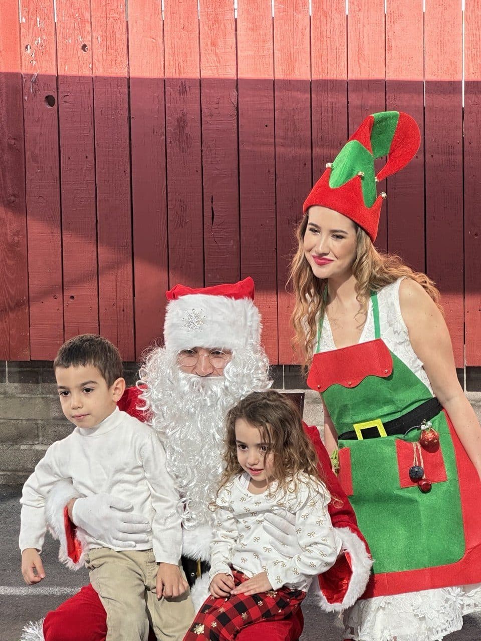 Two children pose happily with a Santa performer and an elf entertainer.