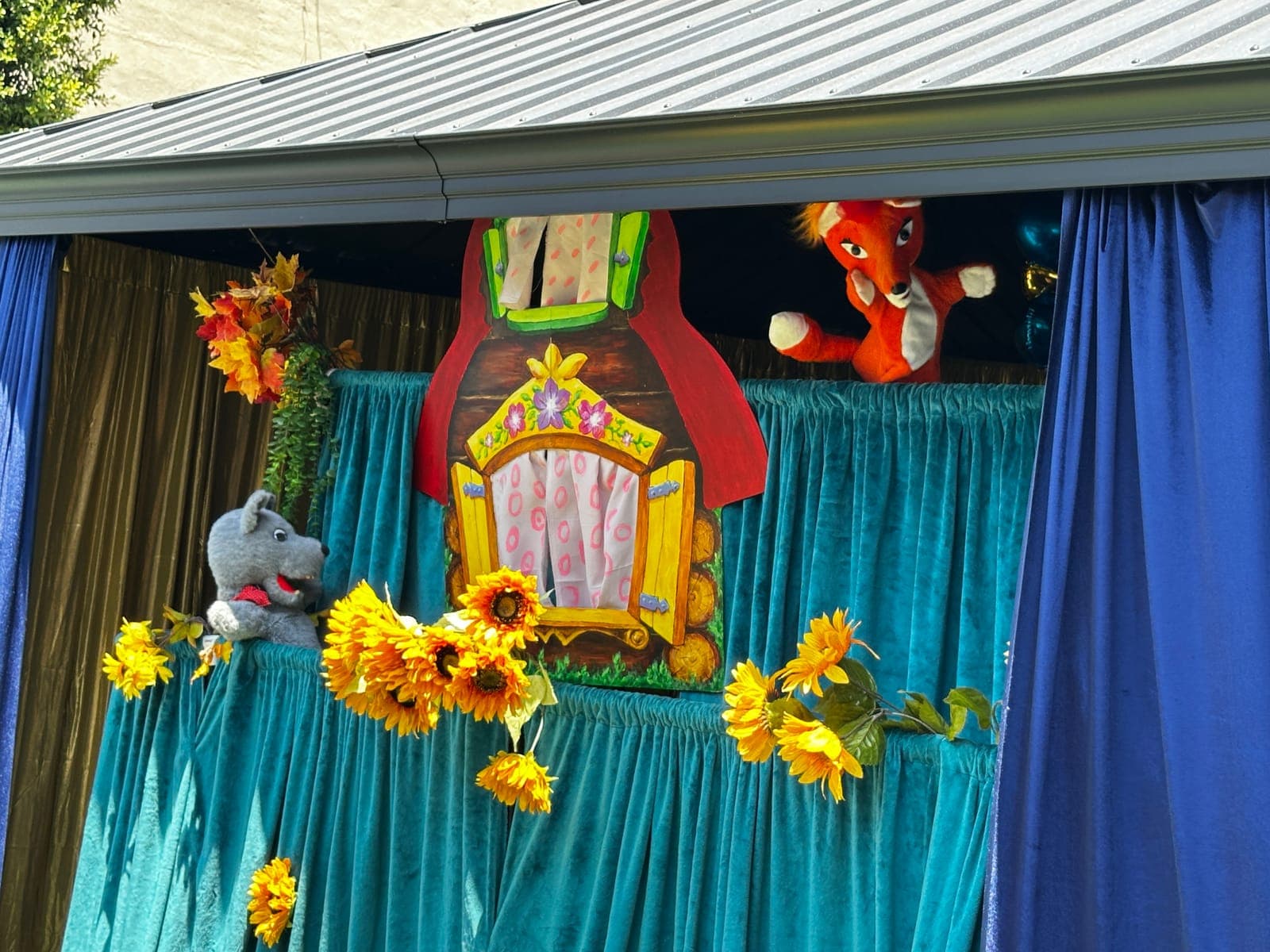 Fox and wolf characters pop up at the window of a hand-painted log-cabin set strung with sunflowers.
