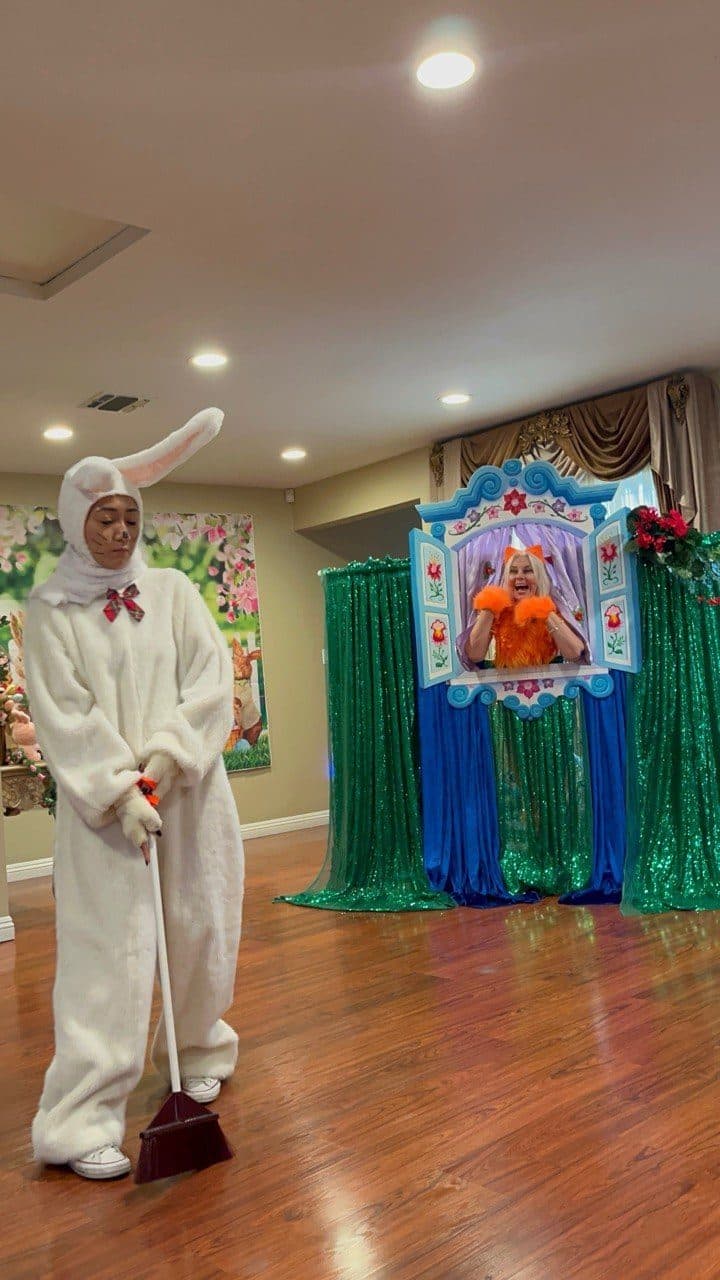 A rabbit-costumed actor sweeps the stage while a fox character looks on.
