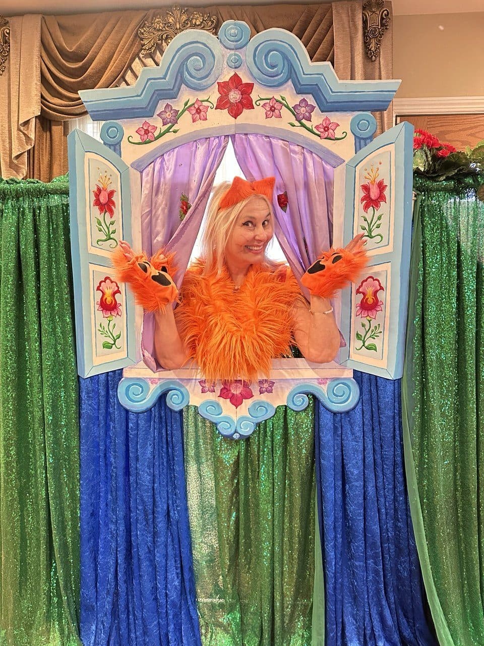 A smiling performer in a bright fox costume poses in a decorative window frame.